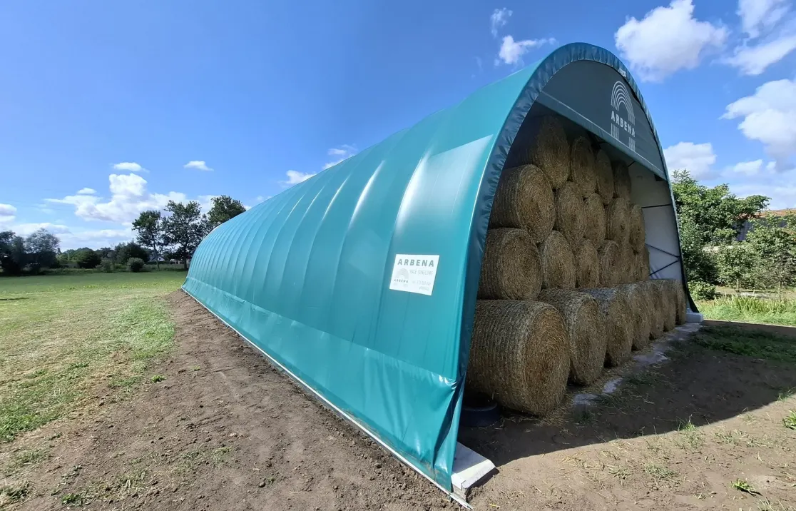 Green ARBENA shelter filled with round bales