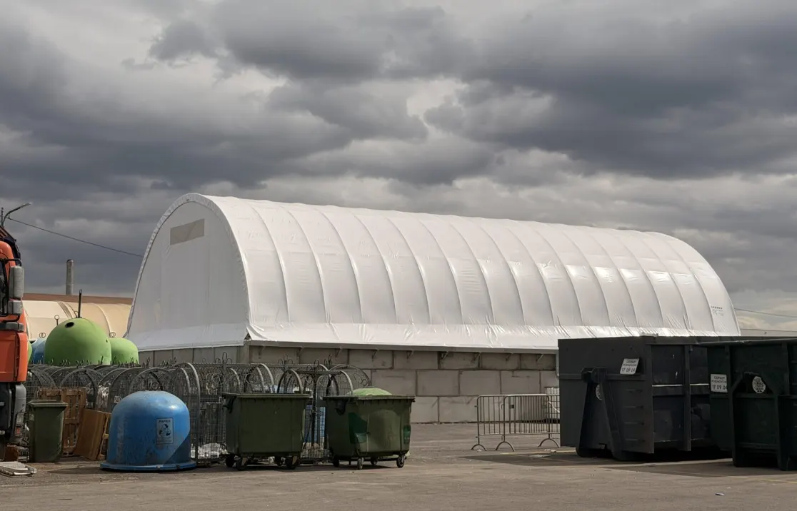 White ARBENA arch building on concrete block walls next to waste containers