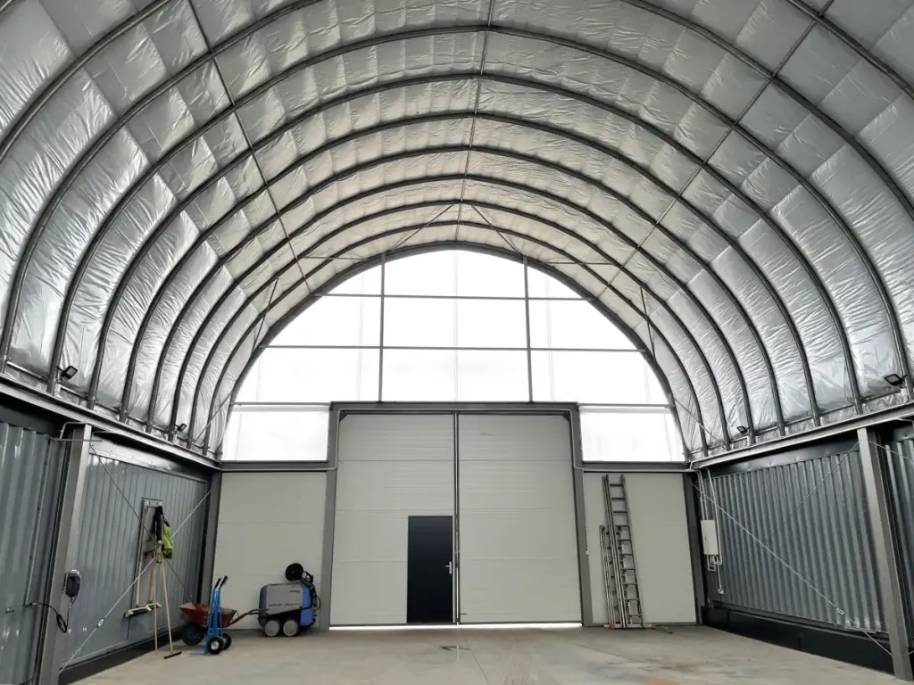 Inside a container canopy: white membrane arch between two rows of containers, gable wall with a door
