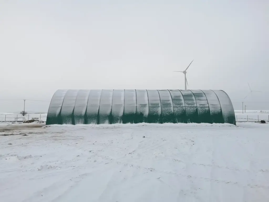 Green ARBENA arch building on snow-covered ground, wind turbine in the background