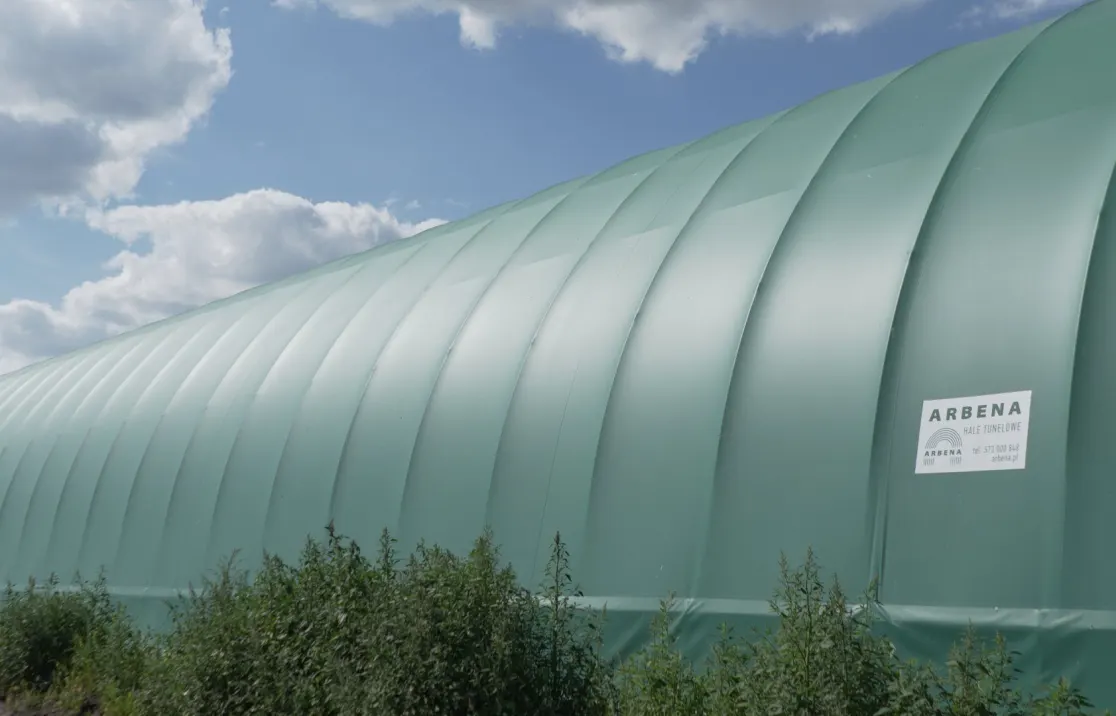 Open gable of a green ARBENA building with straw bales outside