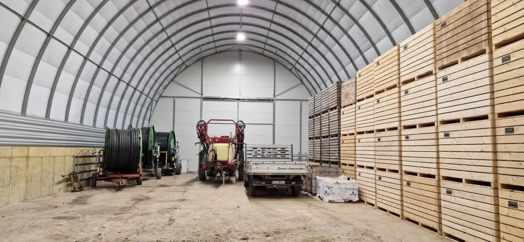Farm storage in an ARBENA building with wooden crates, a tractor and machinery