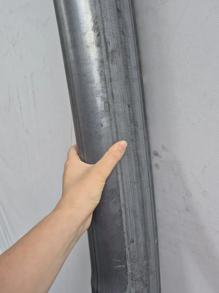 Hand holding a curved oval steel arch profile inside a fabric building